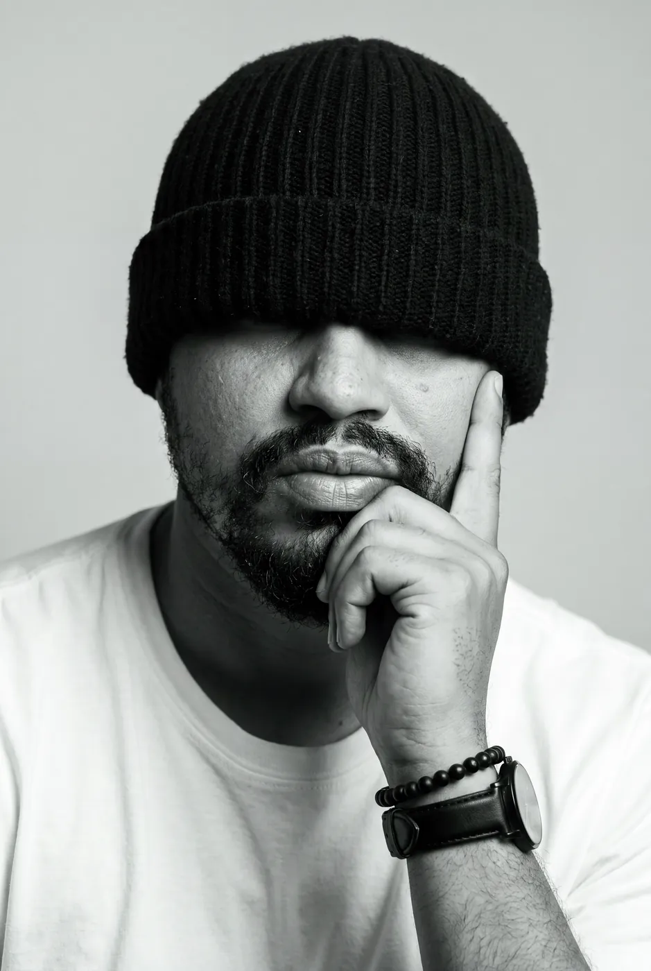 Júnior em preto e branco, gorro cobrindo os olhos, mão no queixo